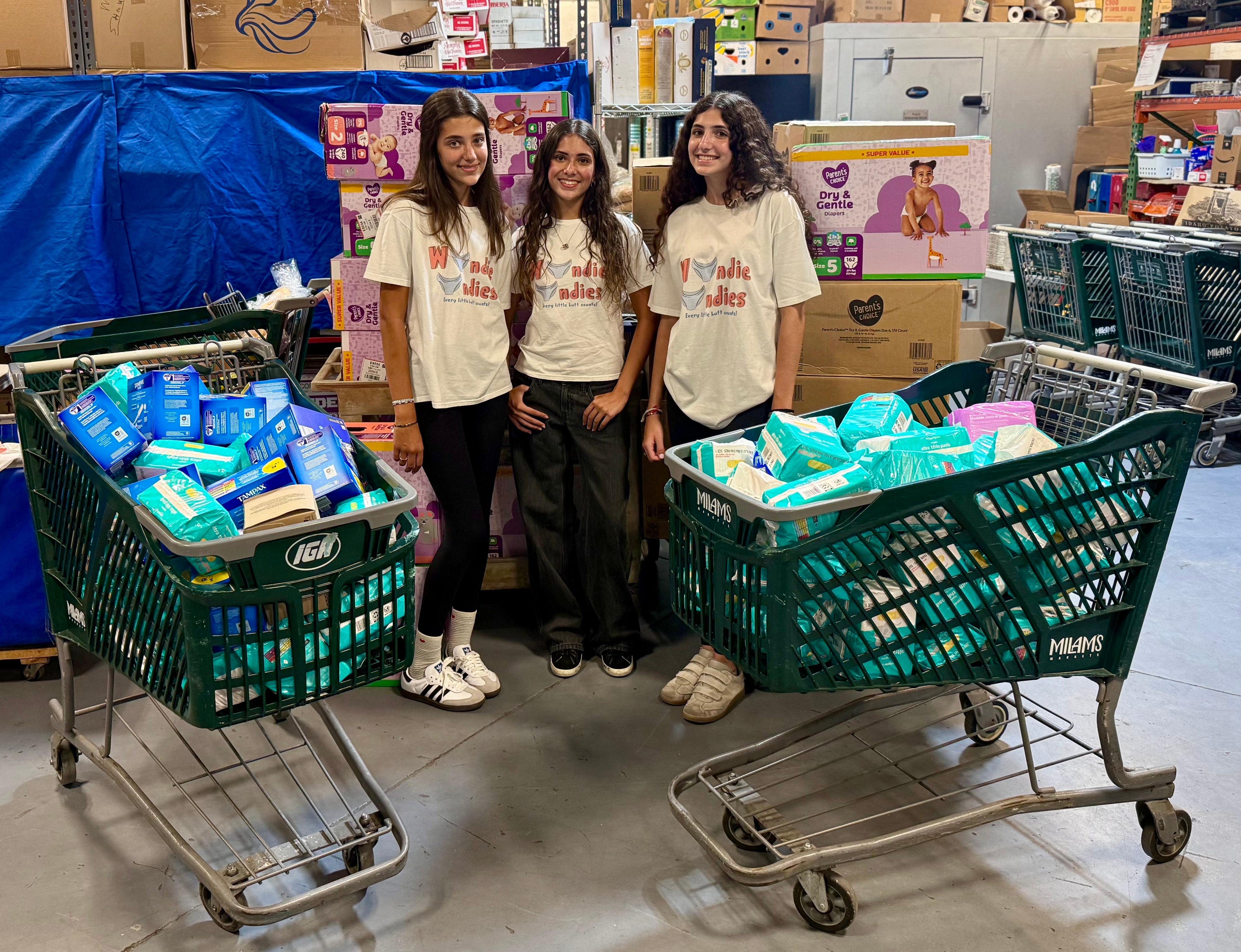 Wundie Undies founders standing with shopping carts full of donated diapers and hygiene products in a warehouse